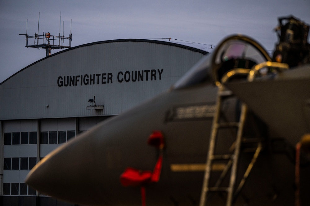 F-15E Strike Eagle on the flightline at Mountain Home Air Force Base, Idaho, in front of the 366th Fighter Wing 'Gunfighter Country' hangar at dawn — relevant to veteran homebuyers PCSing to MHAFB
