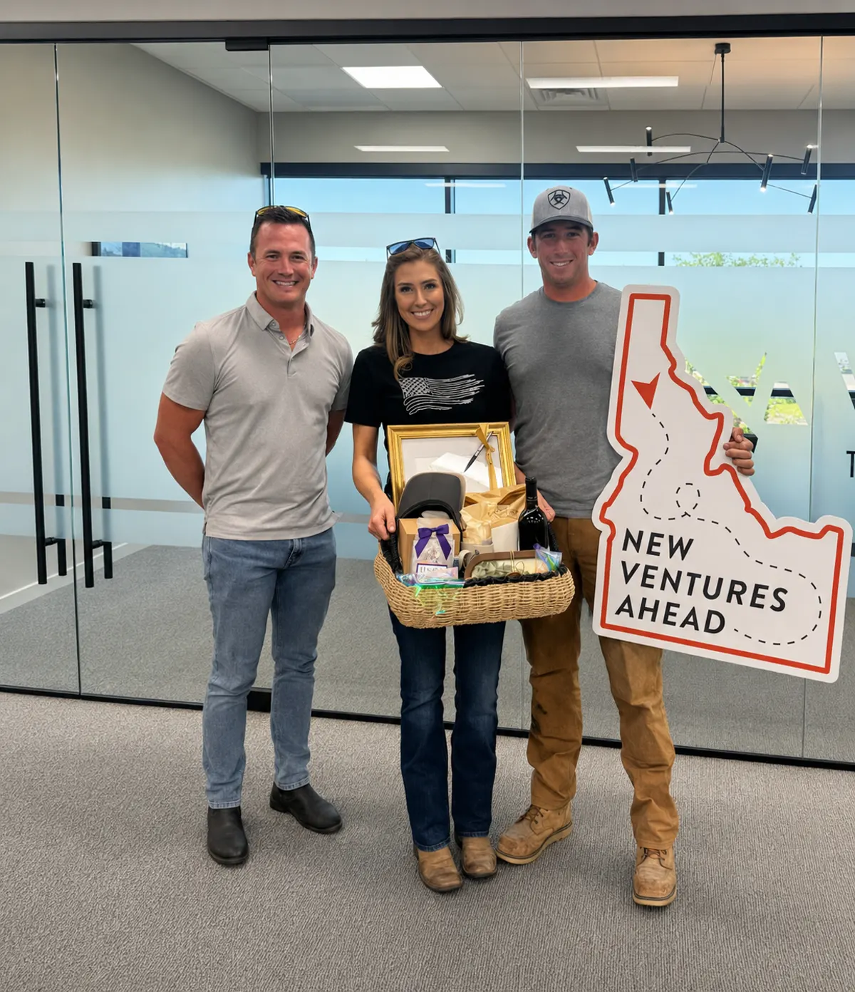 Clients with a Good News Realty Group agent holding an Idaho-shaped New Ventures Ahead sign and a welcome basket
