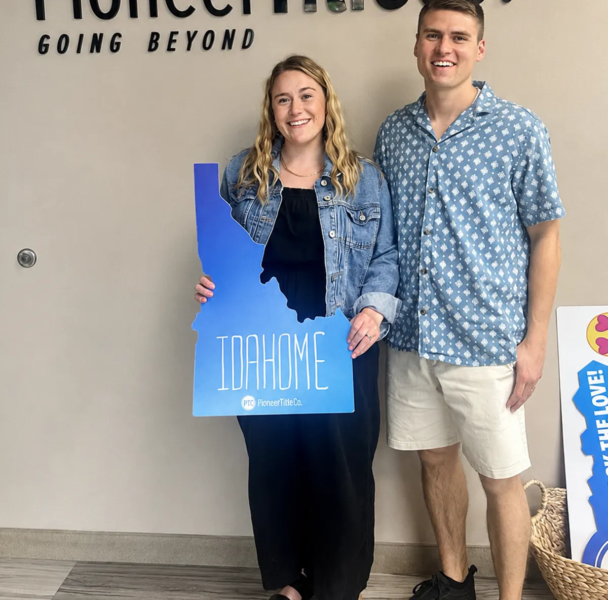 Two new homeowners holding a blue Idaho-shaped Idahome sign at their closing