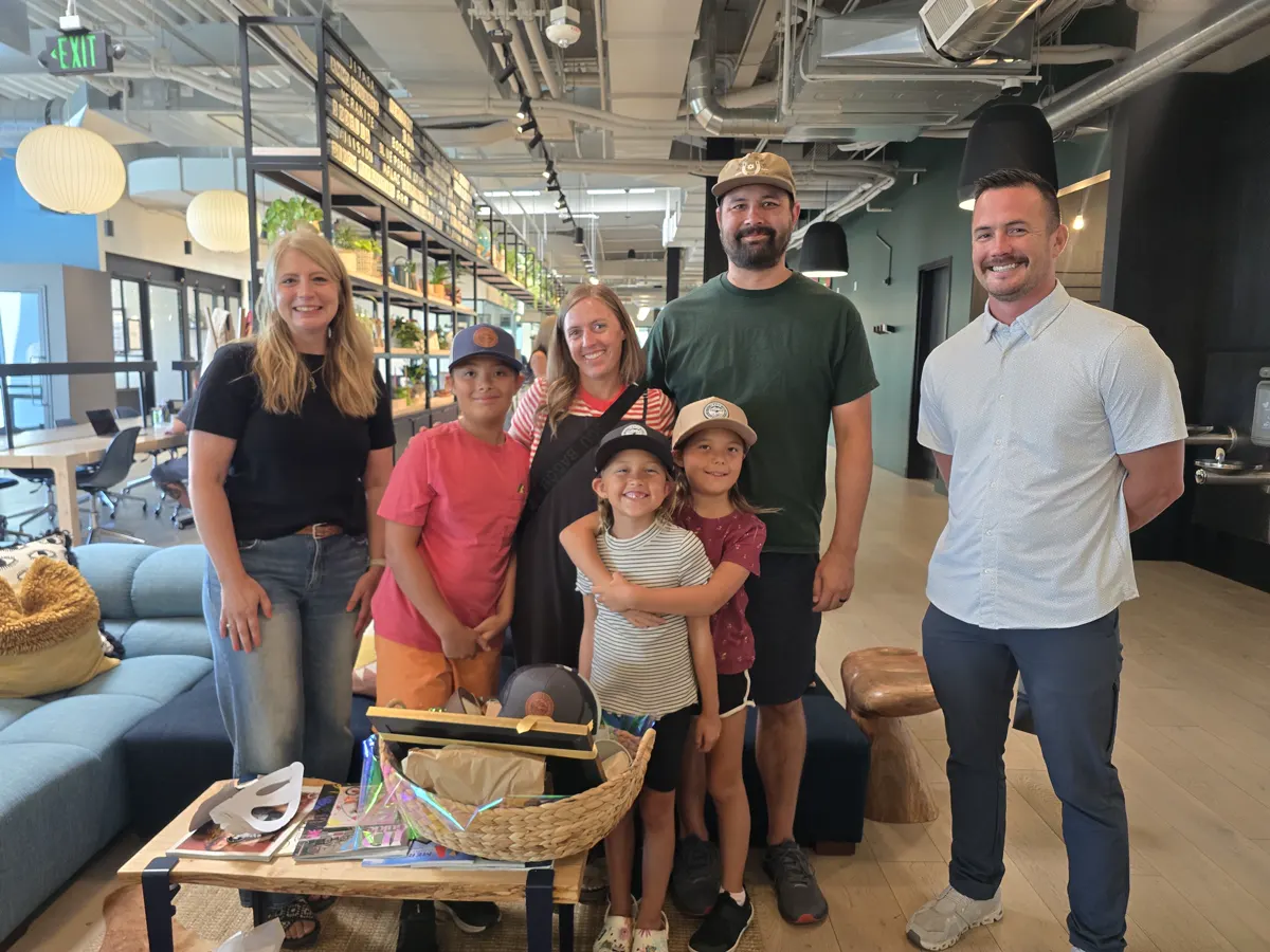 A family of six with a Good News Realty Group agent and a welcome basket in the brokerage office