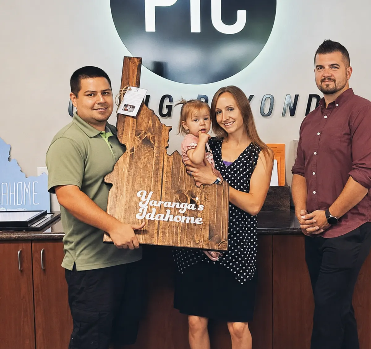 A family holding a wooden Idaho-shaped sign that reads Idahome at their closing