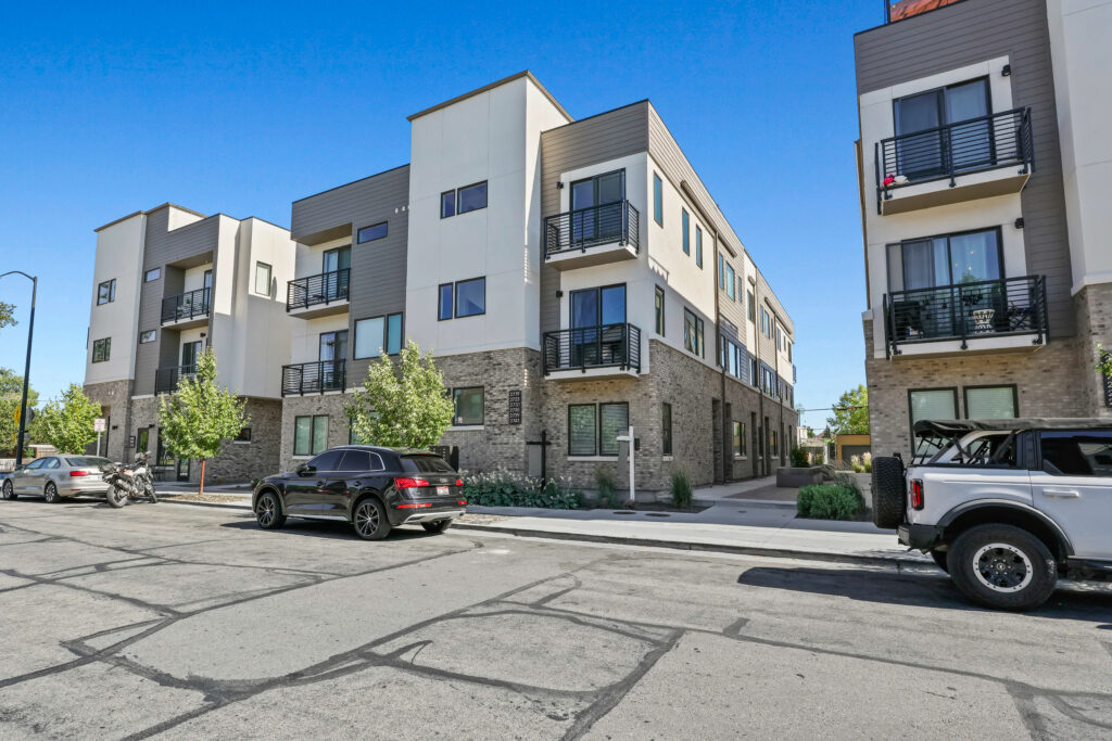 Corner Perspective – Stewart Ave Townhomes - Good News Realty Group Angled view of townhomes with clean streets, parked cars, and modern balconies.