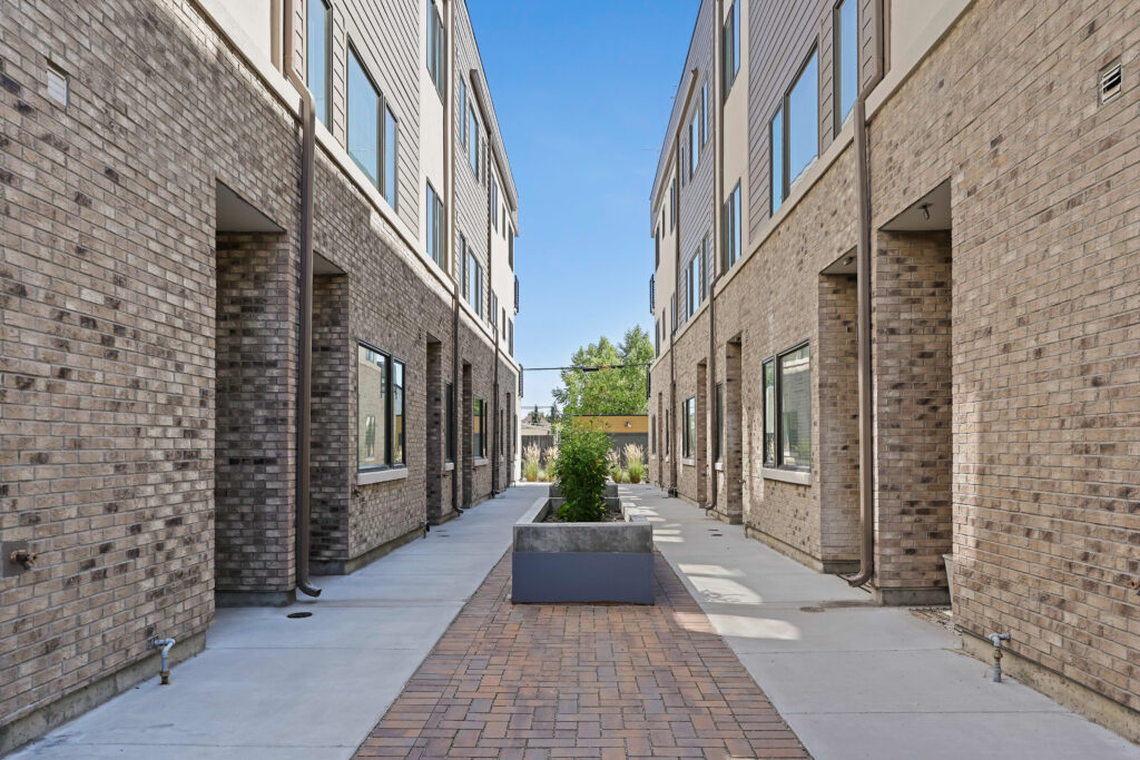 Interior Courtyard – Stewart Ave Homes - Good News Realty Group Brick walkway flanked by modern townhomes with inset doorways and windows.