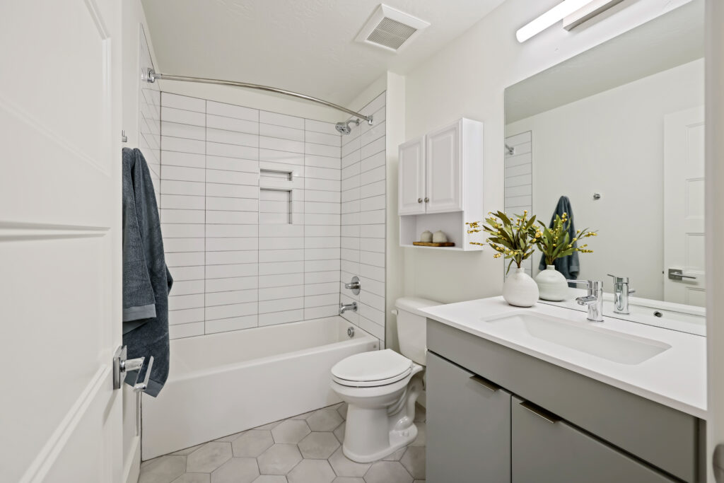 Stylish Full Bathroom - Good News Realty Group Full bathroom with modern vanity, framed artwork, green towels, and marble-look shower tile.