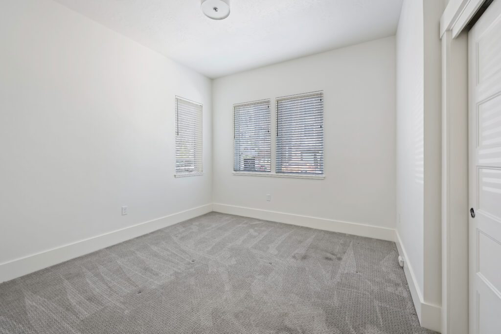 Secondary Bedroom – Blank Canvas - Good News Realty Group Unfurnished room with beige carpet and twin windows with blinds.