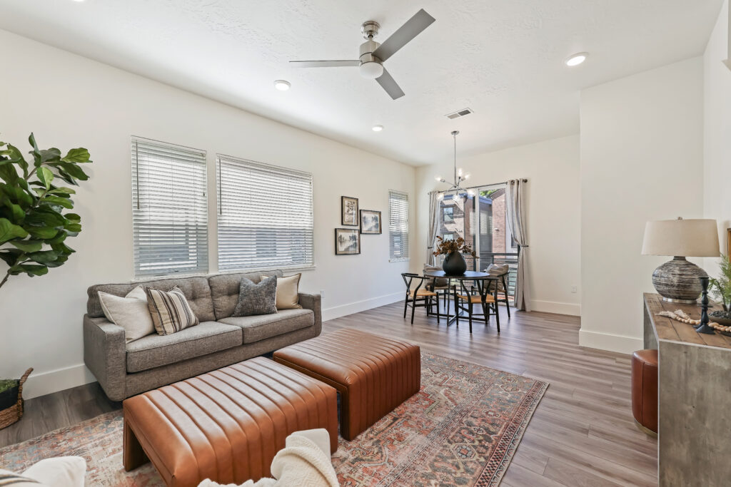 Living and Dining Room Combo - Good News Realty Group Cozy living room with tufted couch, leather ottomans, and dining nook under modern lighting.