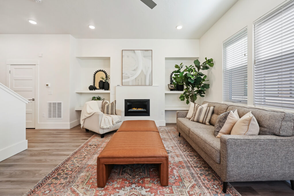 Living Room with Fireplace Focal Point - Good News Realty Group Neutral-toned living room with fireplace, large windows, and decorative shelving.