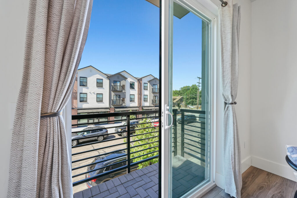 Balcony Access from Dining Area - Good News Realty Group Sliding glass doors open to a private balcony with street and townhome views.