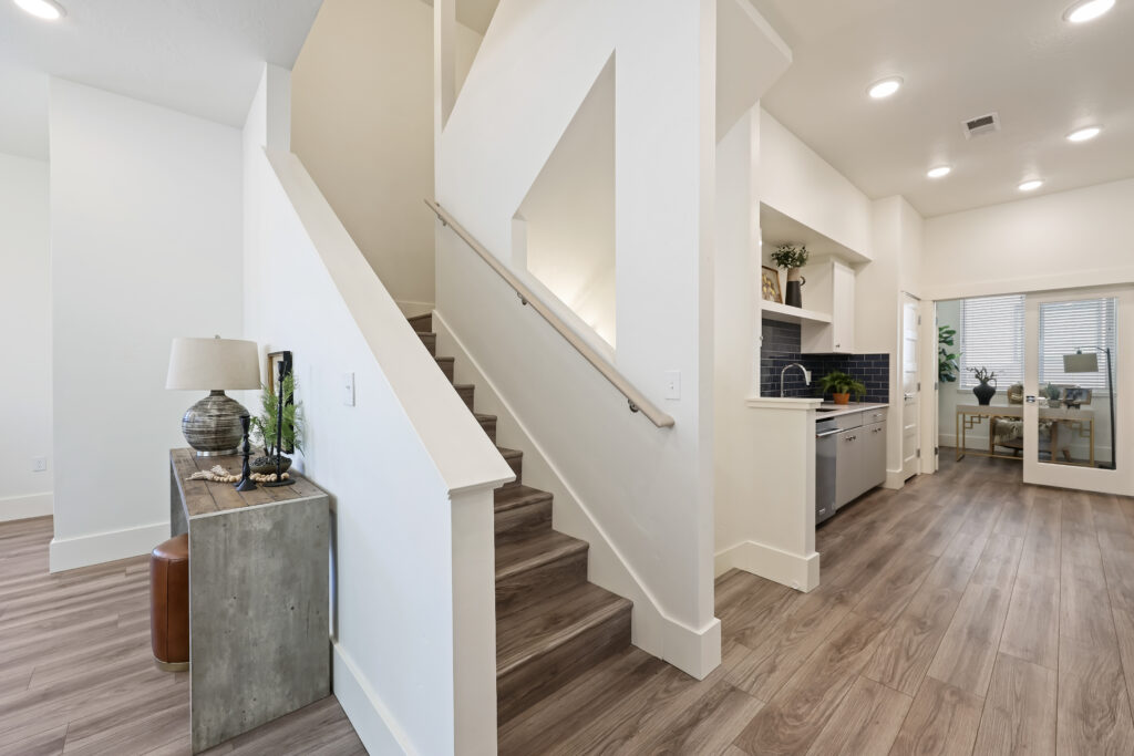 Stairway and Hallway Connection - Good News Realty Group Modern staircase near kitchen with wood floors and decorative console.