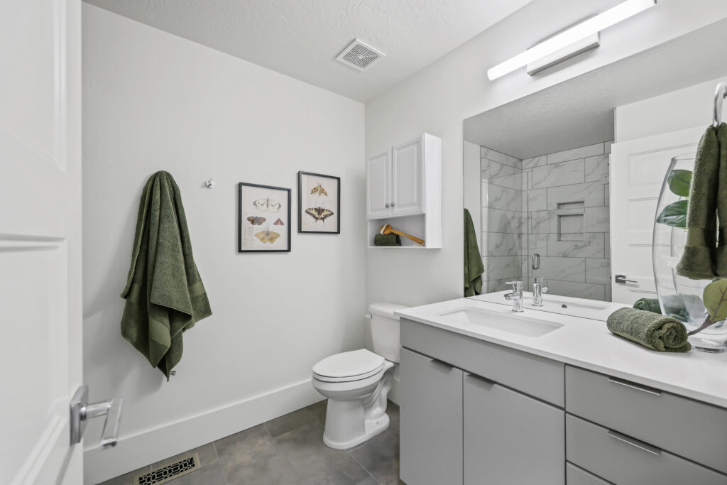 Stylish Full Bathroom - Good News Realty Group Full bathroom with modern vanity, framed artwork, green towels, and marble-look shower tile.
