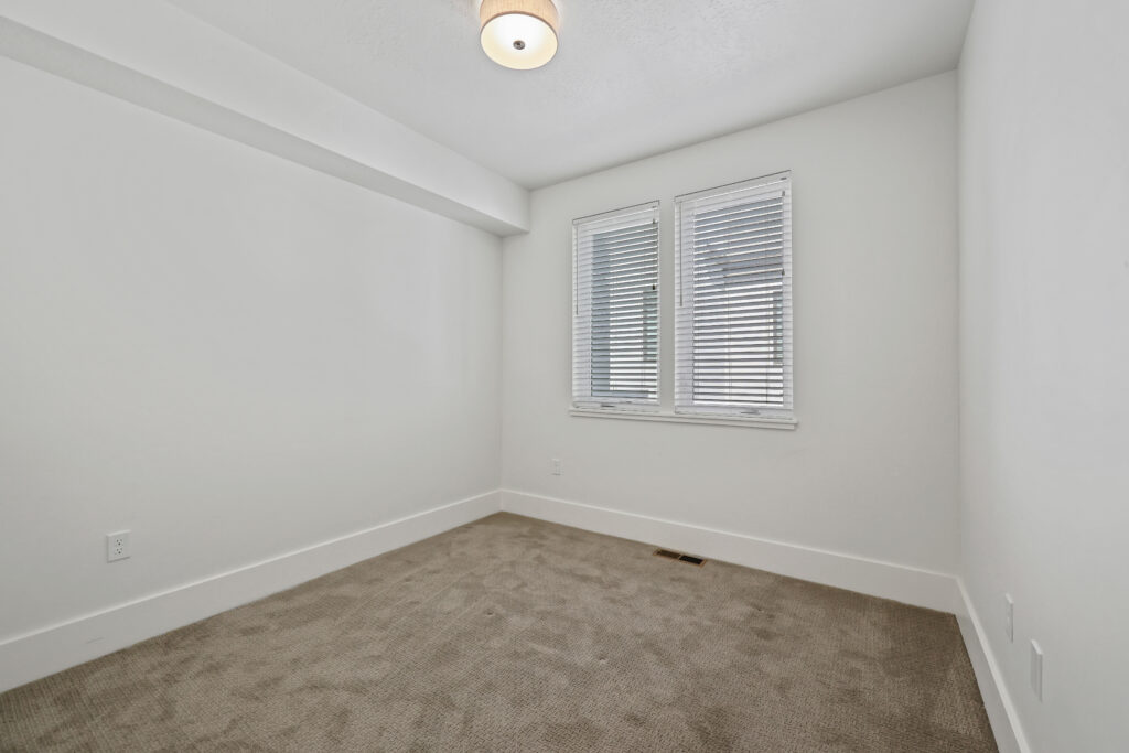 Secondary Bedroom – Blank Canvas - Good News Realty Group Unfurnished room with beige carpet and twin windows with blinds.