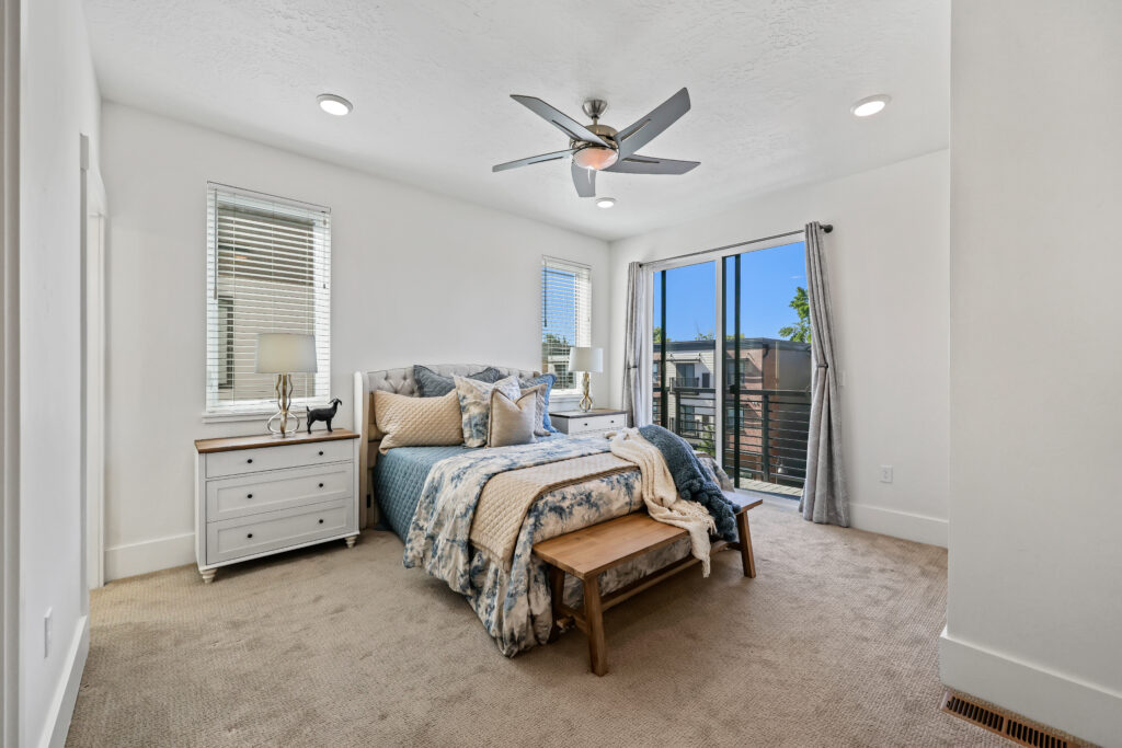 Primary Bedroom with Balcony Access - Good News Realty Group Spacious bedroom with ceiling fan, plush bedding, and sliding doors to a balcony.
